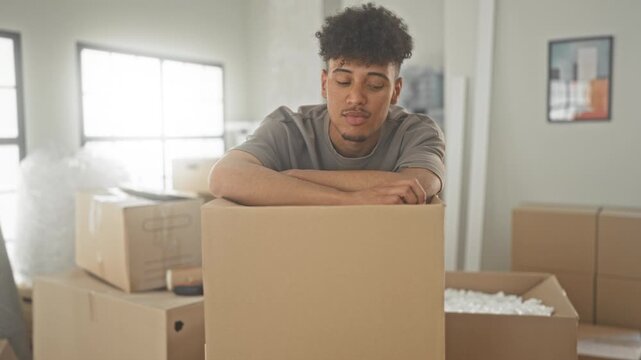Man holding keys up in his hand above moving boxes inside a building, leaning on a cardboard box and smiling; moving day joy.