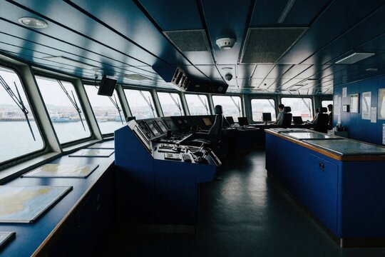 Ship bridge with navigation controls and crew working. Officers monitor radar and charts on a vessel at sea. Harbor view from ship command center.