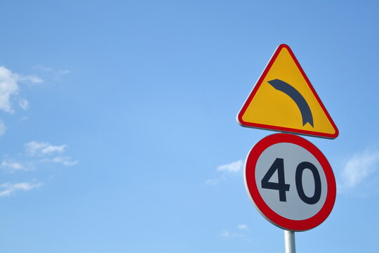 Yellow and red warning road sign for sharp bend with 40 speed limit against blue sky backdrop