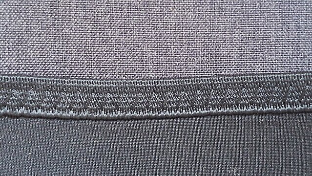 Dark gray fabric texture featuring detailed zigzag stitch pattern surface macro