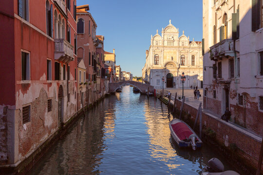 Narrow canal with a small bridge, moored boats and traditional Venetian buildings in Venice, Italy.