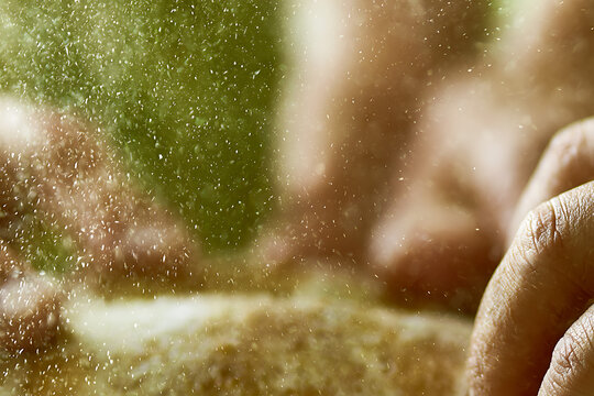A close-up artistic image of a hand interacting with a misty outdoor environment, with sunlight filtering through water droplets or particles in the air. The soft focus, natural light, and green backg