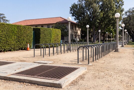 Empty bicycle racks on a dirt path near a building and trees