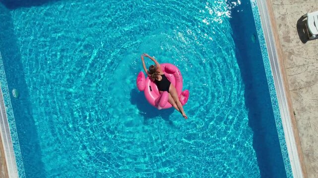 Aerial drone view of beautiful woman on flamingo pool float in pool. Summer holidays
