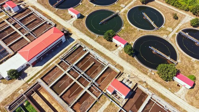 An aerial view shows a water treatment facility with round and rectangular tanks. Buildings with red roofs surround the tanks. Clean water is being processed here. The area is well-organized.