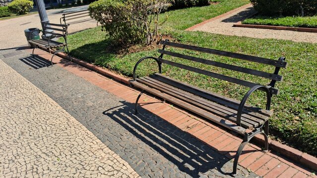 Empty wooden park benches sitting on a sunny stone paved pathway