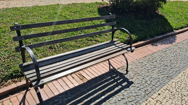 Empty wooden park bench resting on a sunny outdoor brick path