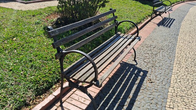 Empty wooden bench sits gracefully beside a sunny cobblestone park pathway