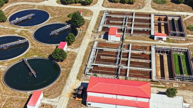 The scene shows a water treatment plant with large circular tanks and several buildings. The area is open with green patches and clear skies. Activity is ongoing during daylight.