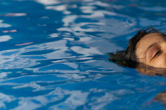Close up shot of young boy floating with eyes closed in rippled blue swimming pool water