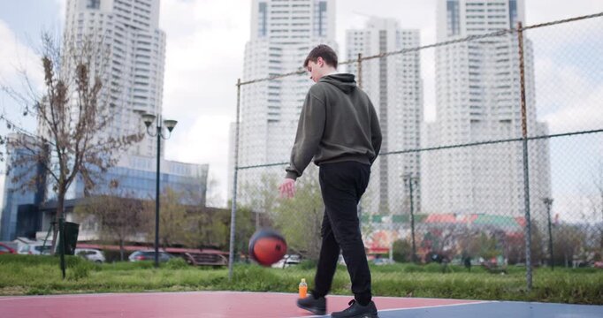 Teenage Boy Dribbling Basketball on Urban Court, Taking a Break and Smiling