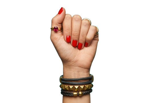 Primer plano de una mano femenina levantada en gesto de pu&ntilde;o con esmalte de u&ntilde;as rojo brillante, anillos dorados y pulseras de cuero apiladas sobre un fondo blanco aislado