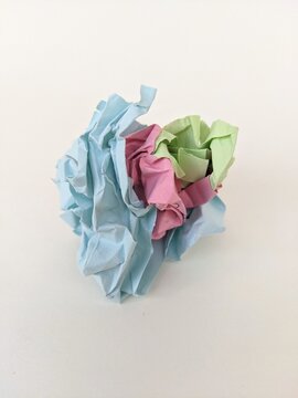 Crumpled colorful paper ball symbolizing creativity, recycling and discarded ideas on plain white background.