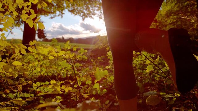CLOSE UP, DOF, LOW ANGLE, SLOW MOTION, LENS FLARE: Woman runs in yellow boots surrounded by glowing autumn leaves and warm sunshine. Vibrant fall color, and authentic outdoor moment in the forest.