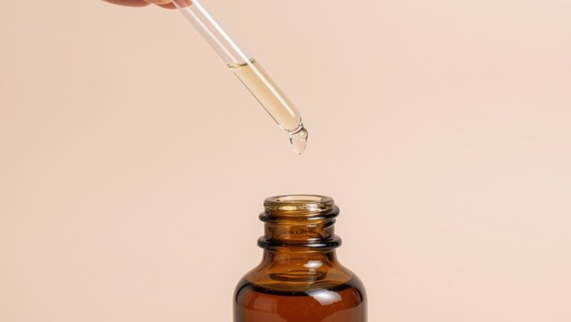 Close-up of a glass dropper with a liquid droplet above an amber pharmaceutical bottle on a neutral background, medical and laboratory concept