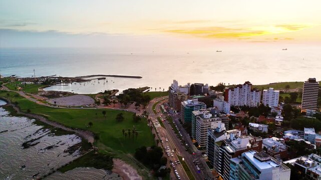 Drone view of Montevideo at sunset, showing the coastal avenue, waterfront buildings, traffic and the R&iacute;o de la Plata under warm evening light.