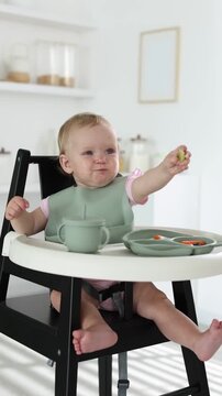 Baby tableware. Cute little child eating food from section plate on high chair at home