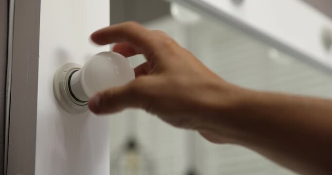 Man replacing light bulb in vanity mirror indoors, closeup