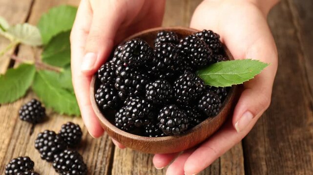 Woman with ripe blackberries at wooden table, closeup