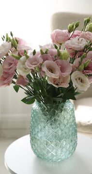 Bouquet of beautiful eustoma flowers in vase on white coffee table indoors, closeup. Camera moving left