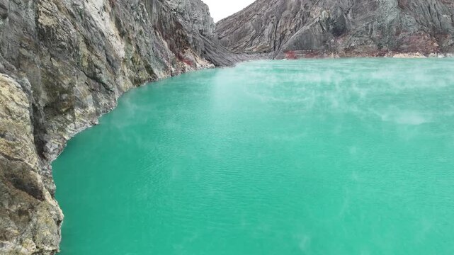 Cinematic aerial flyover above smoking toxic green crater lake showcasing mystical sulfur mist and ancient volcano rocks