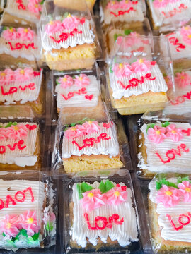 Individual mini cake slice with love writing and pink flower decoration displayed in clear plastic packaging