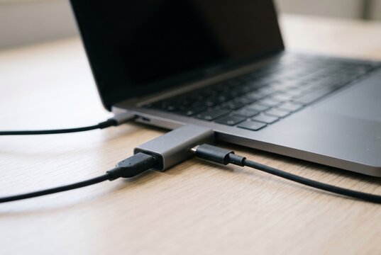 USB data blocker adapter connected to a laptop on a wooden desk representing cybersecurity concept