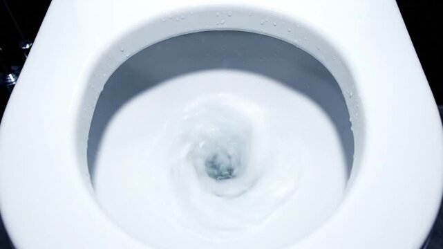 Close up view of clean white toilet flushing water in modern home bathroom interior with indoor plumbing system and hygiene concept