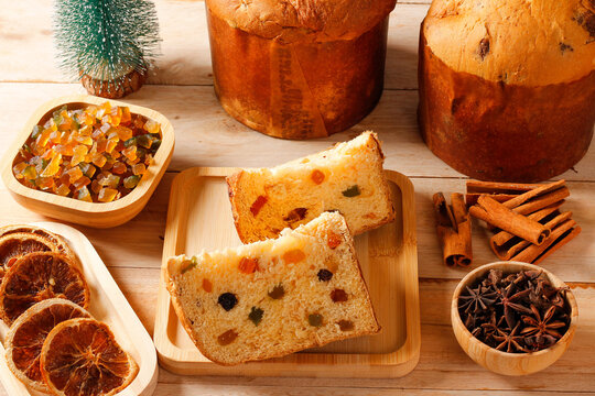 Slices of panettone with candied fruit and raisins, surrounded by dried orange, cinnamon, and star anise on a rustic Christmas tabl