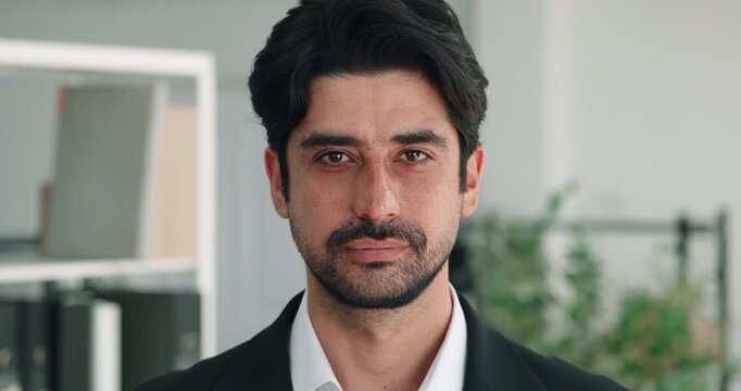 Portrait of Arab businessman faces forward in bright office with serious expression. Focused man holds steady posture presenting professional corporate ethnic