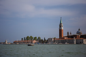 Fototapeta premium San Giorgio Maggiore island with its famous campanile tower and church surrounded by the Venetian lagoon under a cloud-dappled sky.