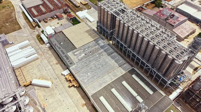 An aerial view shows an industrial site with large silos, a production building, and storage areas. The layout includes several sections and is situated in an open area.