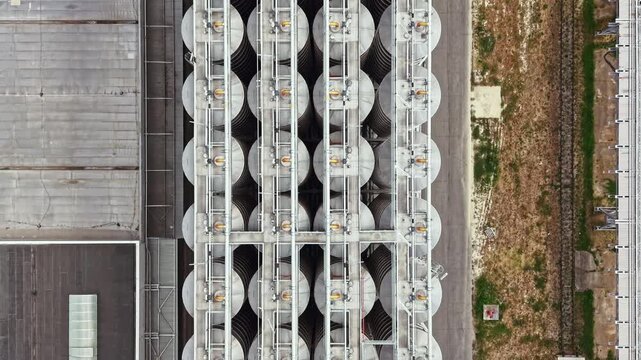 Storage tanks are lined up in neat rows in an industrial area. The view is from above, showing paths and buildings nearby. It is daytime and the area is developed.