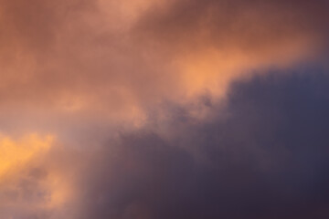 Fototapeta premium Dramatic low-angle view of intense sunset-colored clouds blending from bright orange to dark heavy purple storm masses, creating a perfect mood-driven atmospheric background for scenic nature design.
