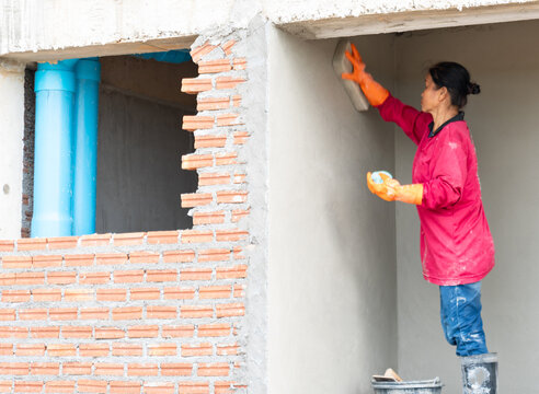 Construction worker smoothing wet plaster on a concrete wall using a float tool inside a building site.