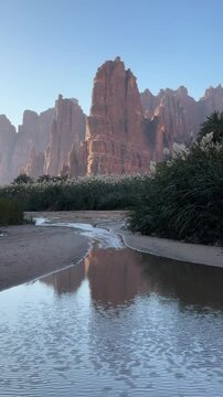 Scenic desert oasis with tall sandstone rock formations reflecting on calm water stream in Wadi Al Disah Tabuk Saudi Arabia