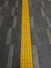Fototapeta premium Yellow tactile paving blocks for visually impaired navigation on pedestrian sidewalk