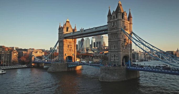Amazing shot of Tower Bridge spans the River Thames. Bathed in golden light during sunset. With the London city skyline and its modern skyscrapers visible in the background against a clear blue sky