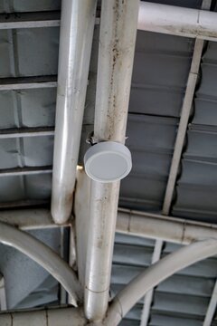 Detail of a round LED ceiling downlight mounted on a steel roof support pipe in a public facility.