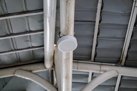 Detail of a round LED ceiling downlight mounted on a steel roof support pipe in a public facility.