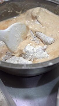 Vertical close up of chef mixing flour coated raw chicken into wet spiced batter in a metal bowl