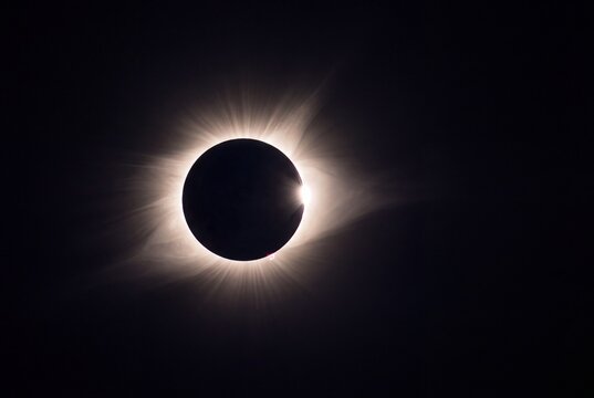 Total solar eclipse with visible corona and bailys beads effect in dark sky