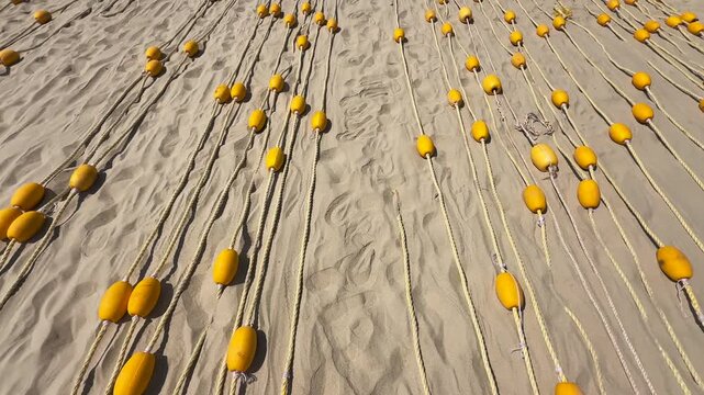 Top View motion above Yellow Oval Buoys on braided rope neatly laid out in parallel on the Beach Sand Pattern