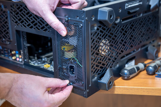 A technician tightens the upper and lower thumb screws of a power supply unit. Tools lie ready beside the computer case. Assembly or upgrade of a desktop computer