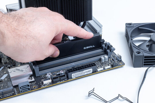 A hand installs G.SKILL RAM modules into an ASUS motherboard. A technician is performing a PC upgrade. A large black CPU cooler fan lies nearby. Pavlodar, Kazakhstan - May 31, 2026