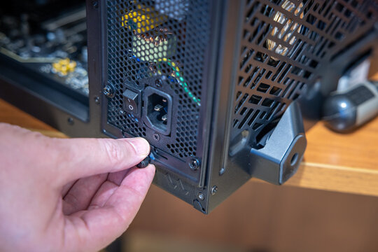 A technician turns the thumb screw that secures a power supply unit in a desktop computer case. The mains socket and power switch are visible on the unit. PC build, upgrade or repair