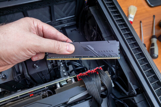 Technician holding DDR memory module above open case of high-end gaming PC. PC assembly or upgrade for high-performance gaming. Rising prices on premium RAM