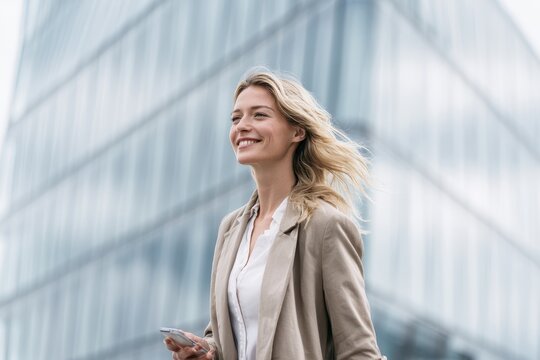 A confident professional woman in a beige blazer smiling while walking outdoors in front of a modern glass office building during the day