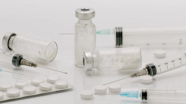 Medical syringes. Glass vials filled with white powder medicine. And pills appearing on a clean white background. representing vaccination, drug abuse, or medical treatment.