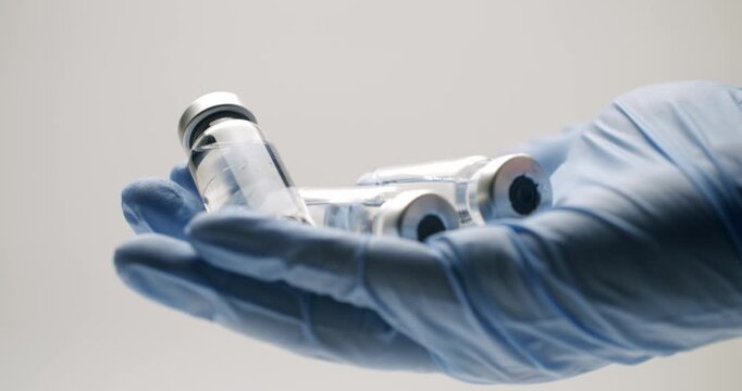Doctor's hand wearing a blue latex glove holding a row of transparent glass vials containing medicine, vaccine or serum for treatment, illustrating pharmaceutical research and healthcare